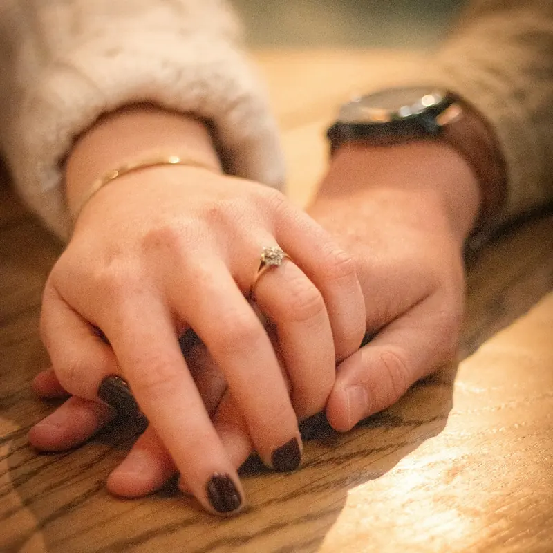 Two hands resting on each other on a wooden table